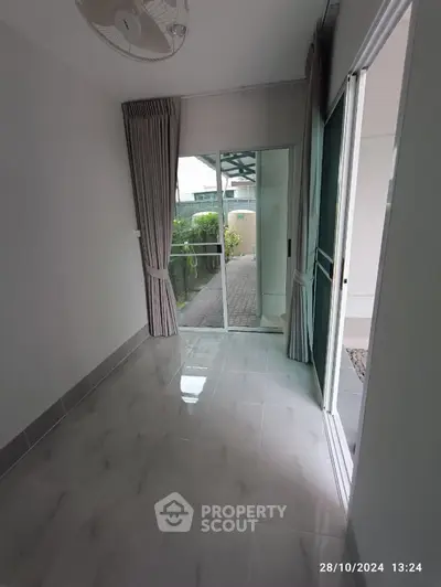 Bright room with sliding glass doors leading to a garden view, featuring elegant curtains and tiled flooring.