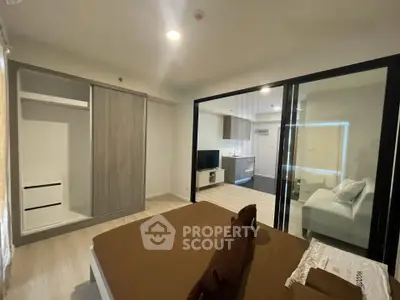 Modern bedroom with sliding glass doors and open view to living area, featuring sleek furniture and neutral tones.