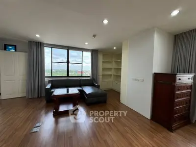 Spacious living room with large window and wooden flooring, featuring elegant furniture and built-in shelves.
