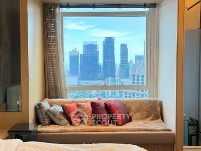 Luxurious bedroom with stunning city view from large window, featuring cozy seating area with plush cushions.