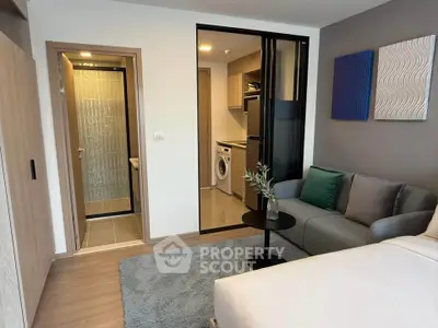 Modern studio apartment with cozy living area and compact kitchen featuring a washing machine.