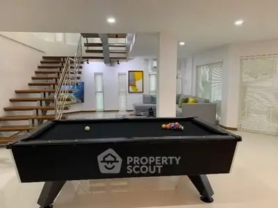 Modern living room with pool table and stylish staircase in open layout home.