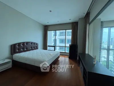 Spacious bedroom with large windows offering city views and elegant wooden flooring.