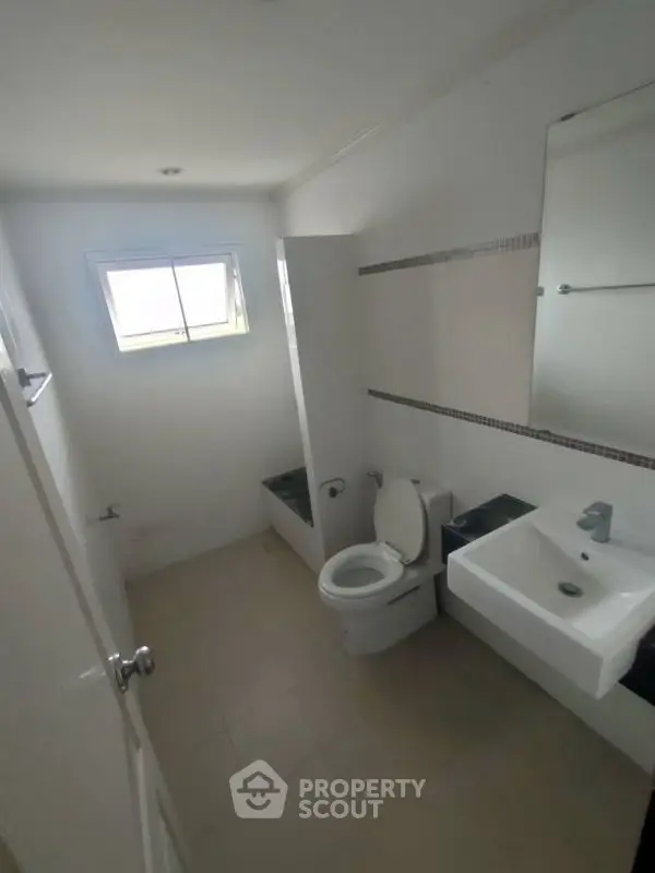 Compact bathroom with modern fixtures and natural light from window.