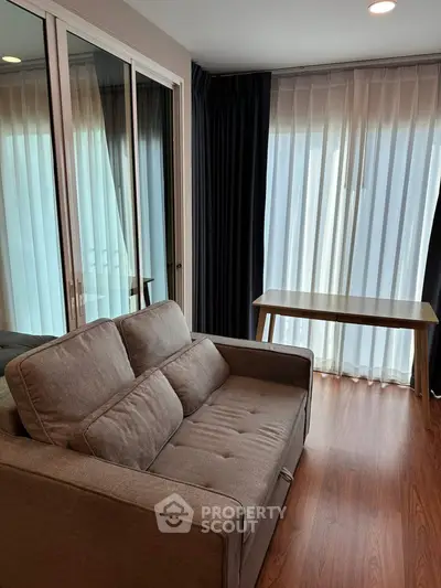 Cozy living room with modern sofa and natural light through large windows.