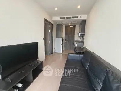 Modern living room with sleek black sofa and flat-screen TV, open to a compact kitchen area.