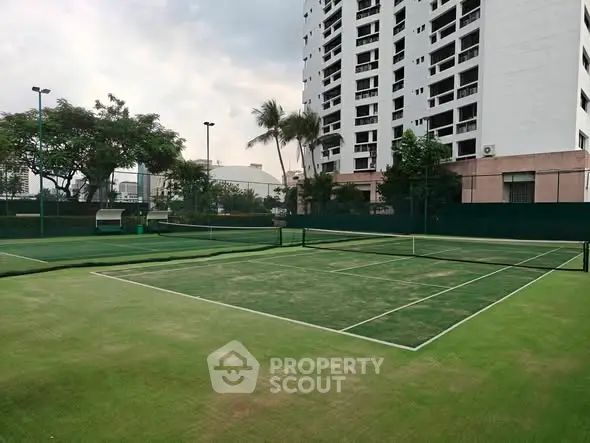 Spacious tennis court with lush green surroundings in a modern residential complex.