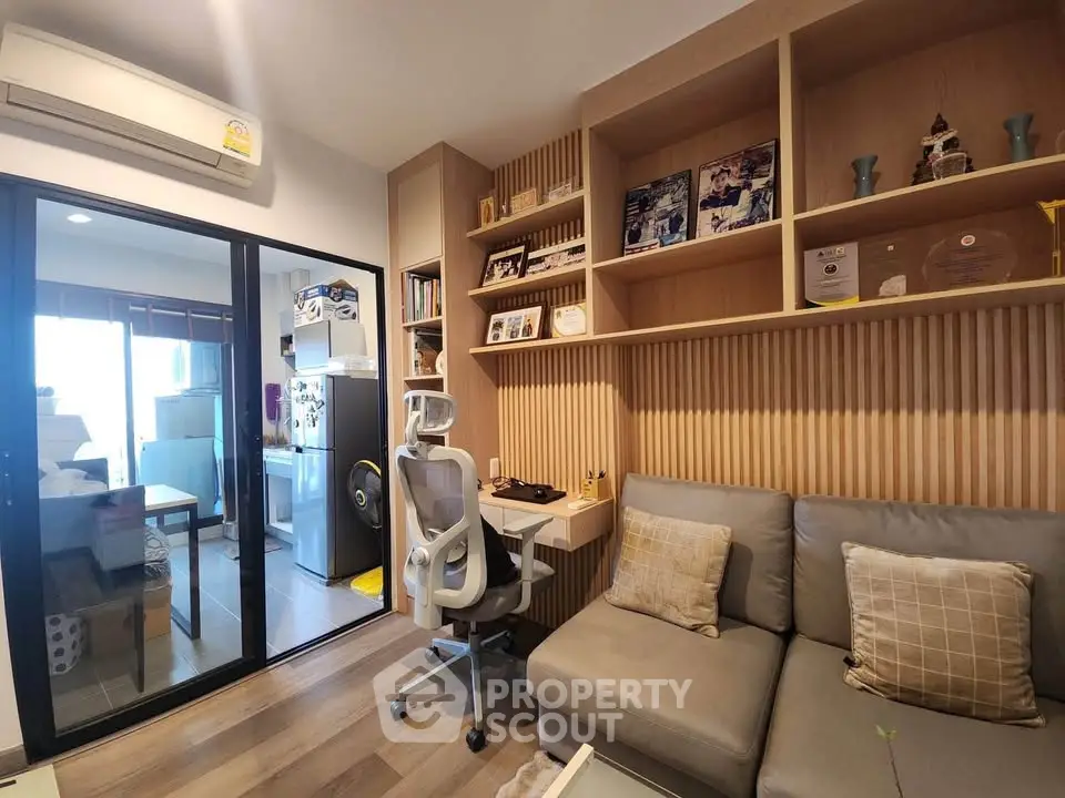 Modern living room with built-in shelves and cozy seating area, adjacent to a compact kitchen.