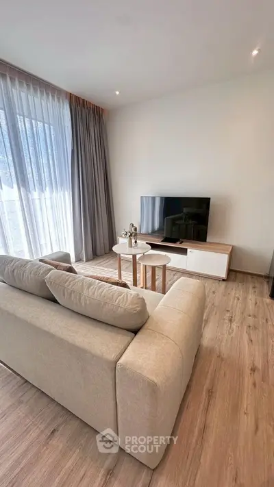 Modern living room with cozy sofa and flat-screen TV, featuring elegant wooden flooring and large windows.