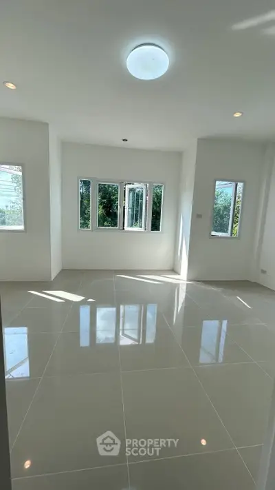 Spacious sunlit room with glossy tiled flooring and large windows offering lush green views.