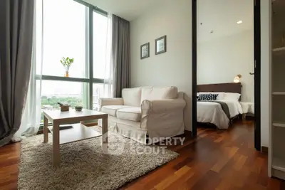 Modern living room with cozy seating and bedroom view, featuring large windows and wooden flooring.