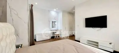 Modern bedroom with stylish decor and wall-mounted TV, featuring a cozy workspace and ample storage.
