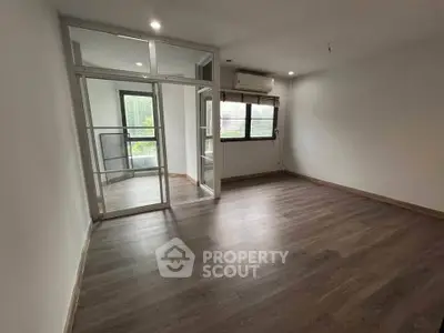 Spacious empty room with wooden flooring and large windows, perfect for customization.