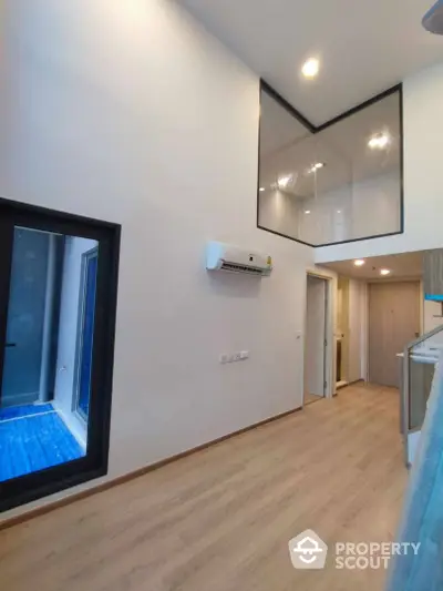 Modern interior with high ceilings and large windows, featuring a sleek air conditioning unit and wood flooring.