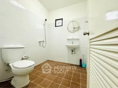 Spacious bathroom with modern fixtures and brown tiled floor, featuring a shower and round mirror.
