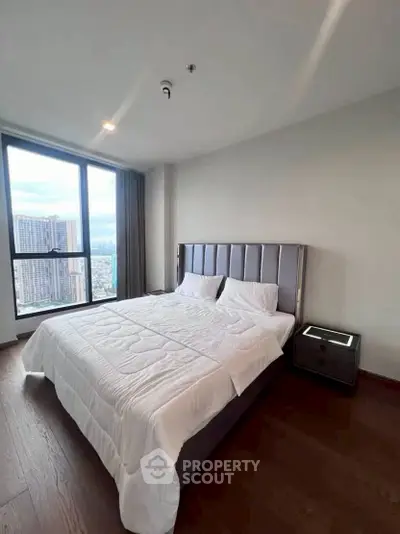 Modern bedroom with large window offering city view, featuring a stylish bed and wooden flooring.