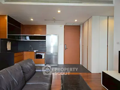 Modern living room with sleek kitchen, leather sofa, and stainless steel fridge in open layout.