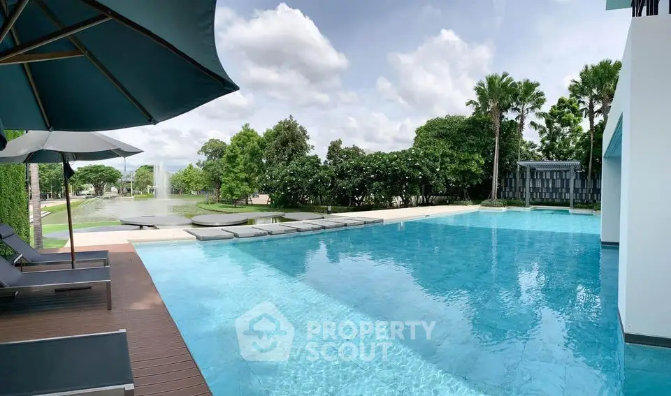 Luxurious outdoor pool with serene garden view and sun loungers, perfect for relaxation.