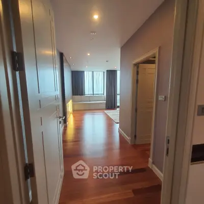 Spacious hallway leading to a bright living area with wooden flooring and large windows.