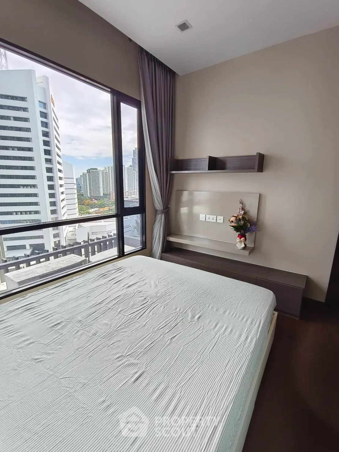 Modern bedroom with city view, featuring large windows and elegant decor.