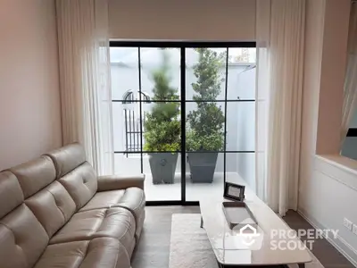 Modern living room with leather sofa and large window overlooking a private patio with greenery.