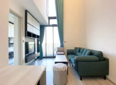 Modern living room with high ceiling and large windows opening to a balcony.