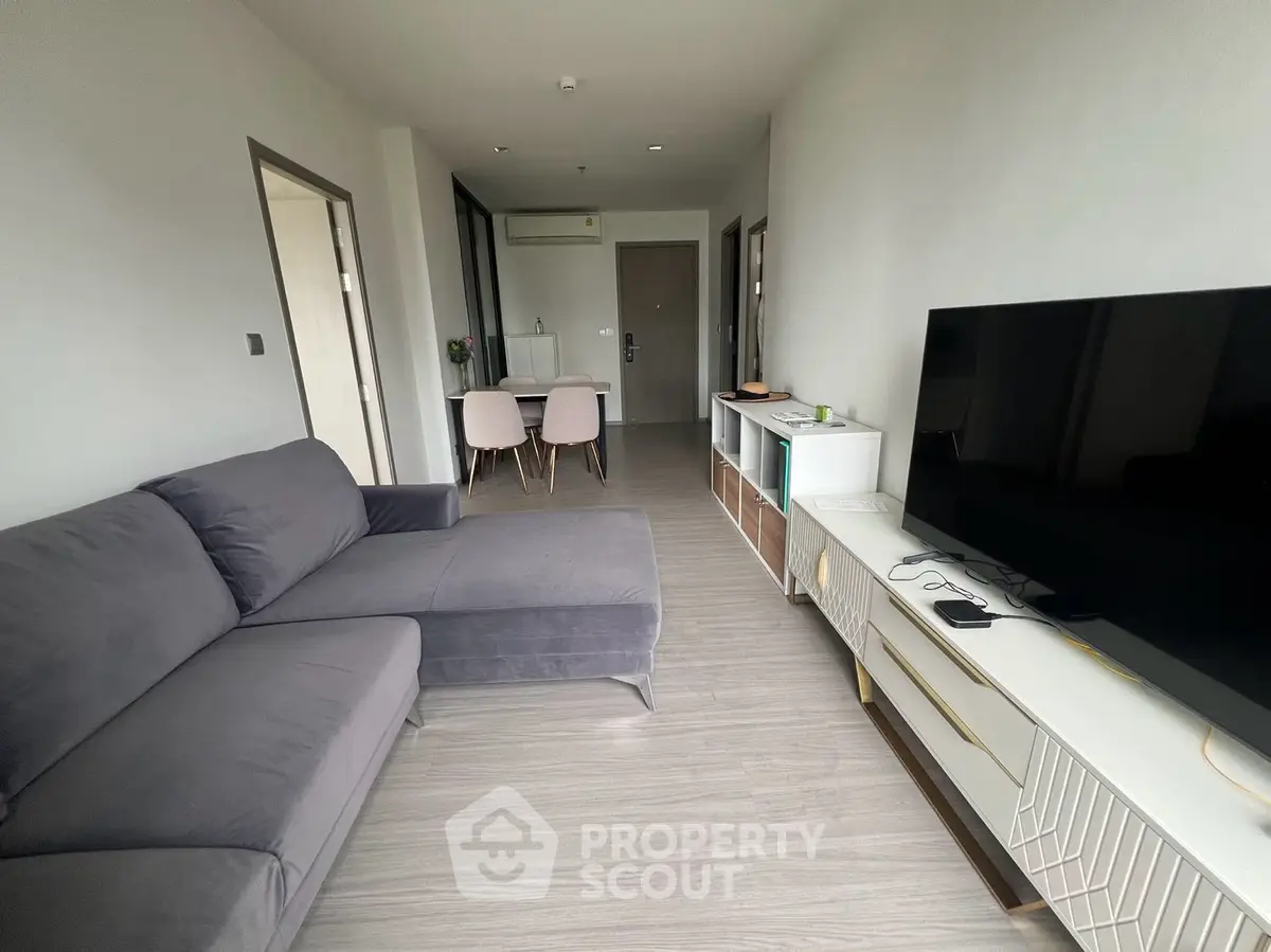 Modern living room with sleek furniture and large TV, open layout leading to dining area.