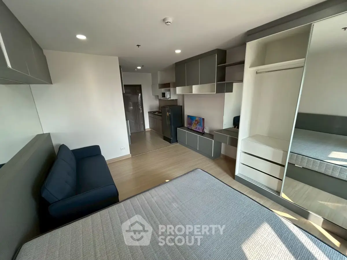 Modern studio apartment with sleek design and ample natural light, featuring a cozy living area and compact kitchen.