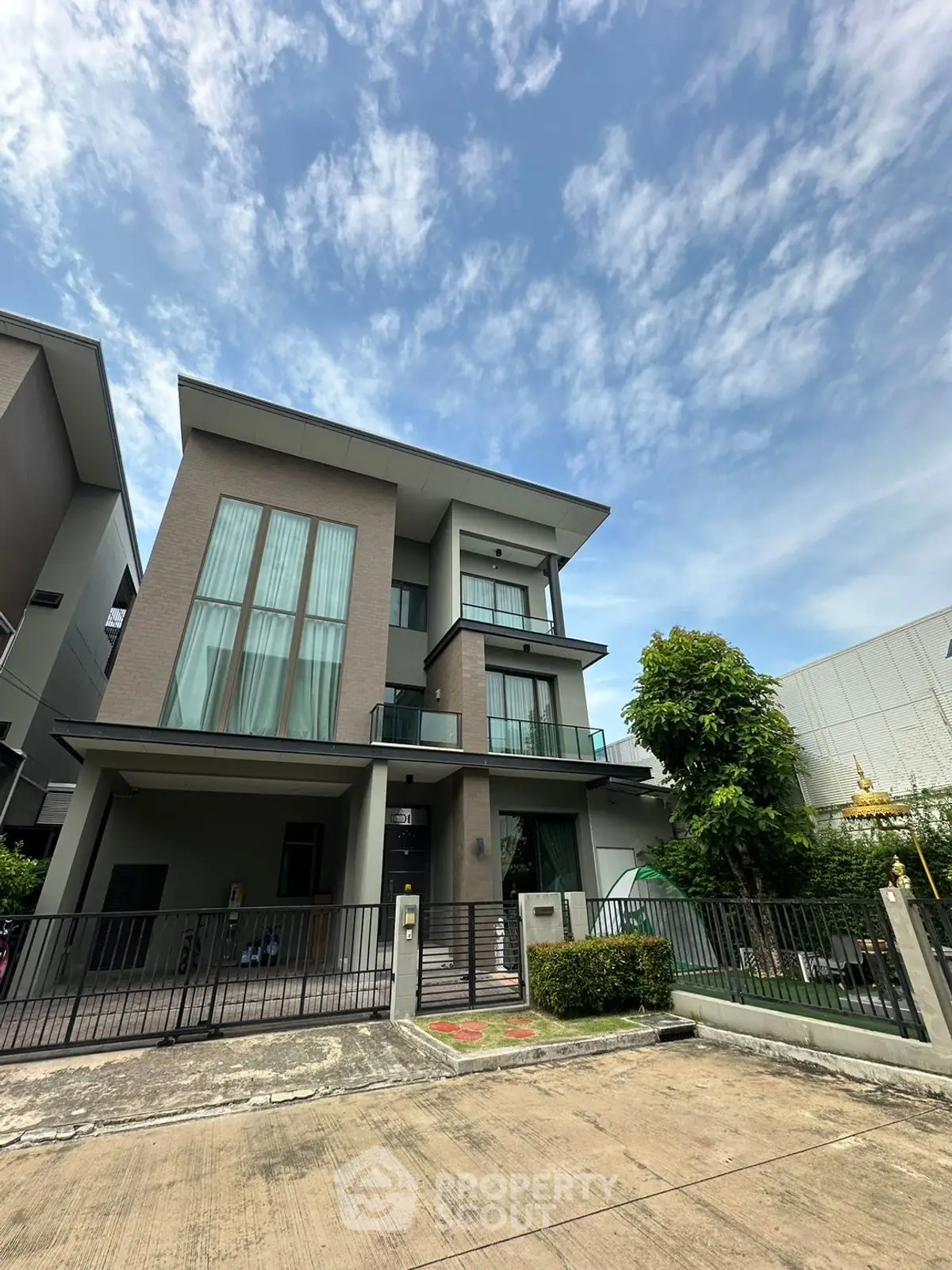Modern three-story house with large windows and a spacious driveway under a clear blue sky.