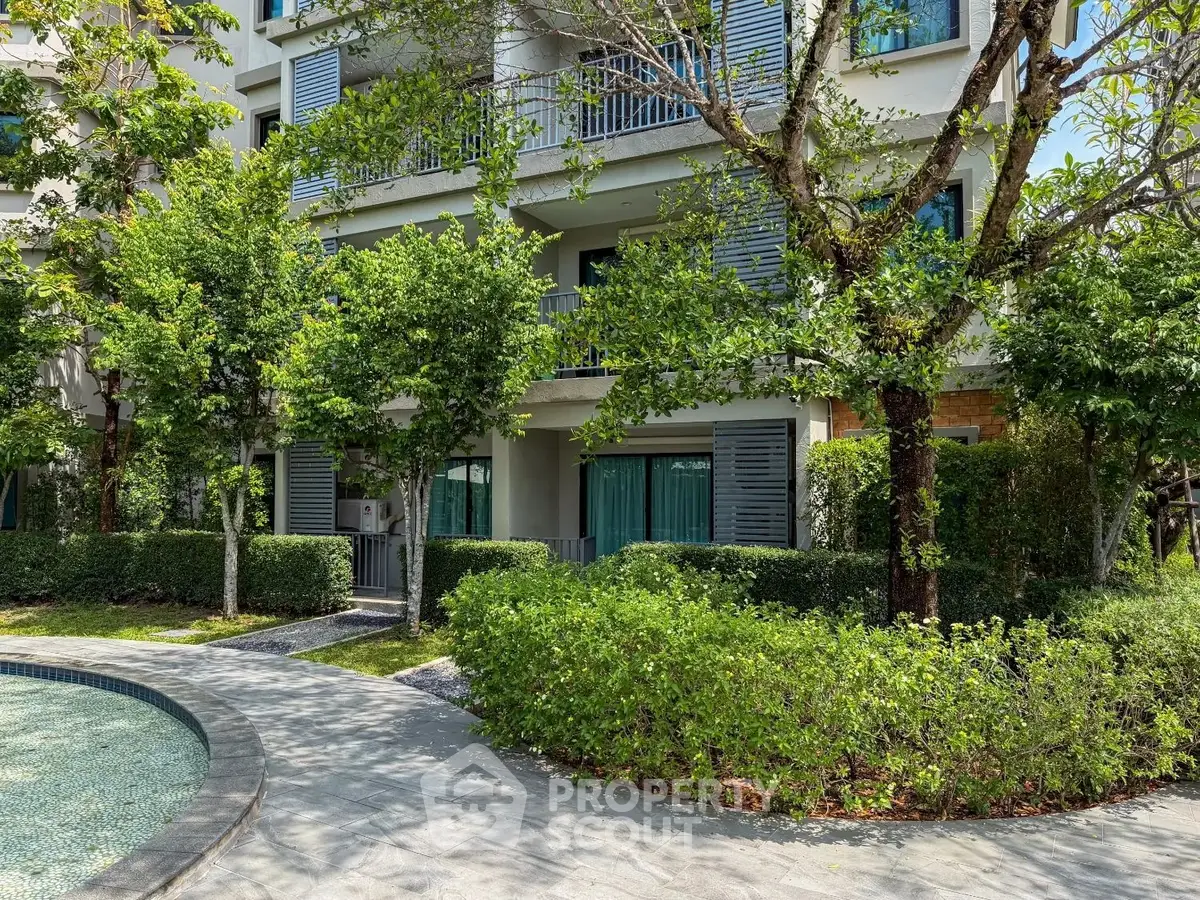 Modern apartment building with lush greenery and poolside view, offering serene living environment.