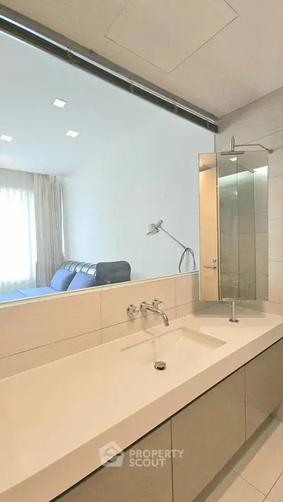 Modern bathroom with sleek design and large mirror, featuring a view into an adjacent room.
