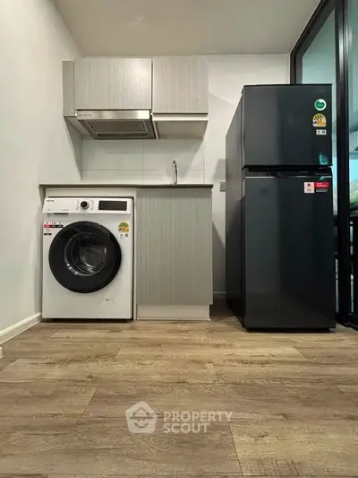 Modern compact kitchen with washing machine and fridge in sleek apartment.