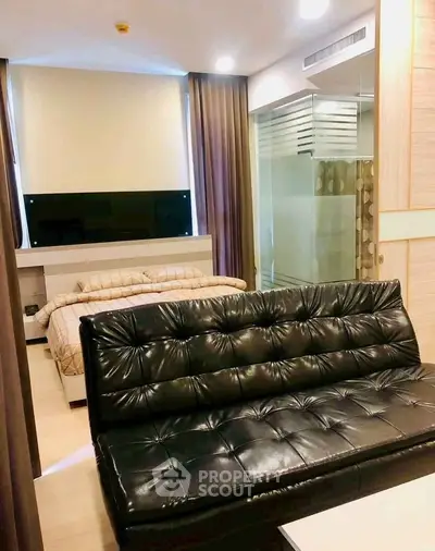 Modern studio apartment with sleek leather sofa and cozy bed, featuring a glass partition for privacy.