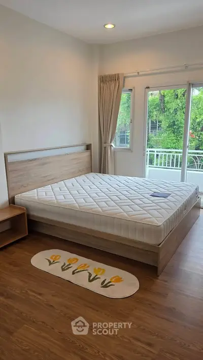 Bright bedroom with large window and wooden flooring, featuring a cozy bed and serene garden view.