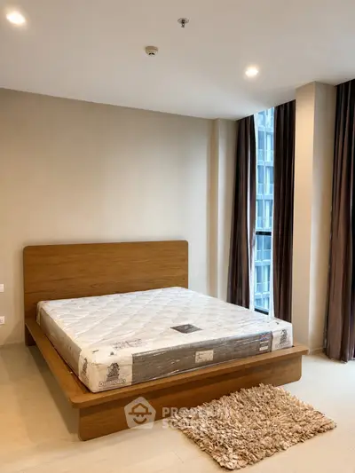 Spacious bedroom with modern wooden bed and large windows offering natural light.