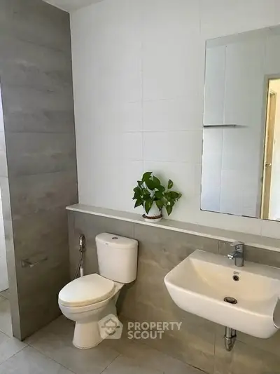 Modern bathroom with sleek fixtures and minimalist design, featuring a wall-mounted sink and a potted plant.