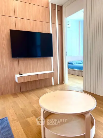 Modern living room with sleek wooden paneling and wall-mounted TV, leading to a cozy bedroom.