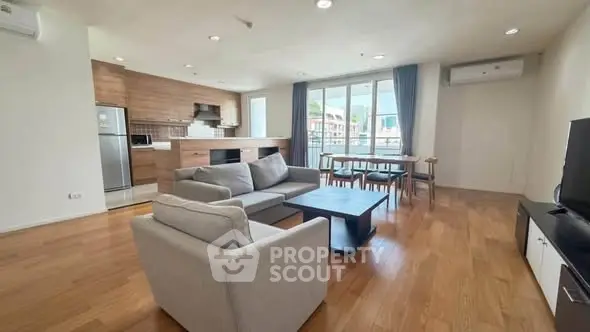 Spacious modern living room with open kitchen and large windows offering natural light.