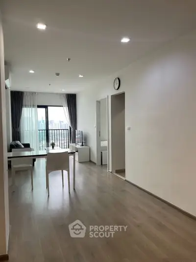 Spacious modern living room with large windows and city view, featuring minimalist decor and wooden flooring.