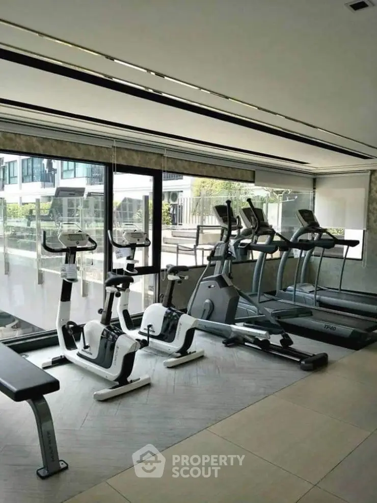 Modern gym with exercise equipment and large windows in a luxury building.