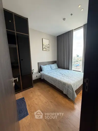 Modern bedroom with large window and city view, featuring wooden flooring and sleek wardrobe.