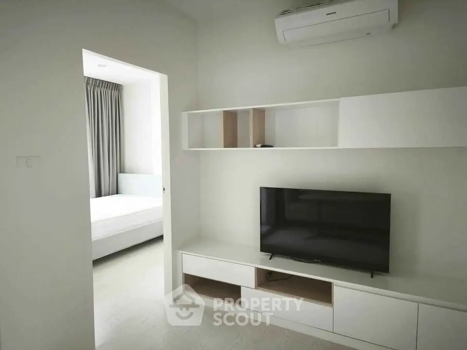 Modern living room with sleek TV unit and view into minimalist bedroom