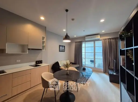 Modern living room with open kitchen and balcony view, featuring stylish furniture and natural light.