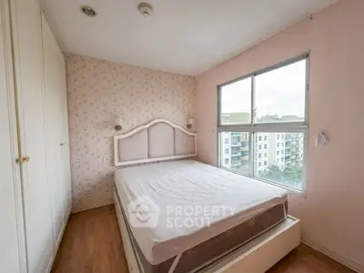 Cozy bedroom with large window and floral wallpaper, offering a serene view of nearby buildings.
