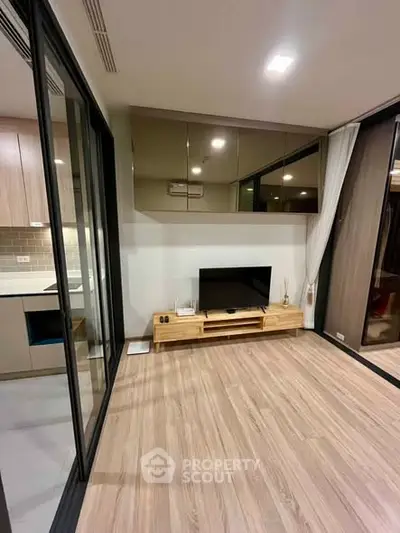 Modern living room with sleek wooden flooring and built-in entertainment unit, adjacent to a stylish kitchen.