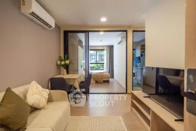 Modern living room with open layout, cozy seating, and view into bedroom and kitchen.