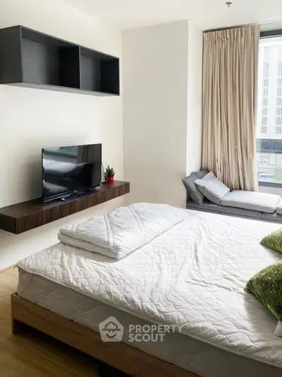 Modern bedroom with cozy bed, wall-mounted TV, and large window with city view.