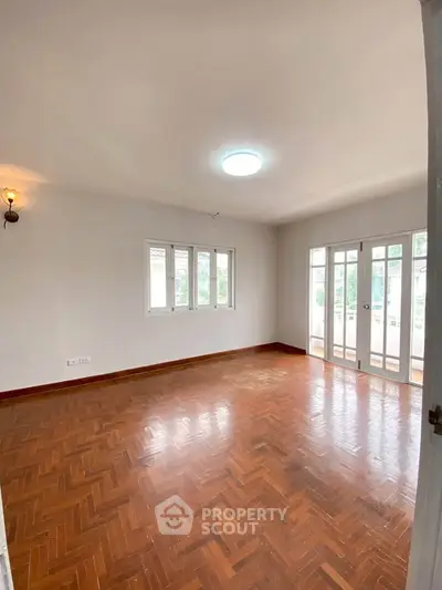 Spacious empty living room with wooden flooring and large windows for natural light.