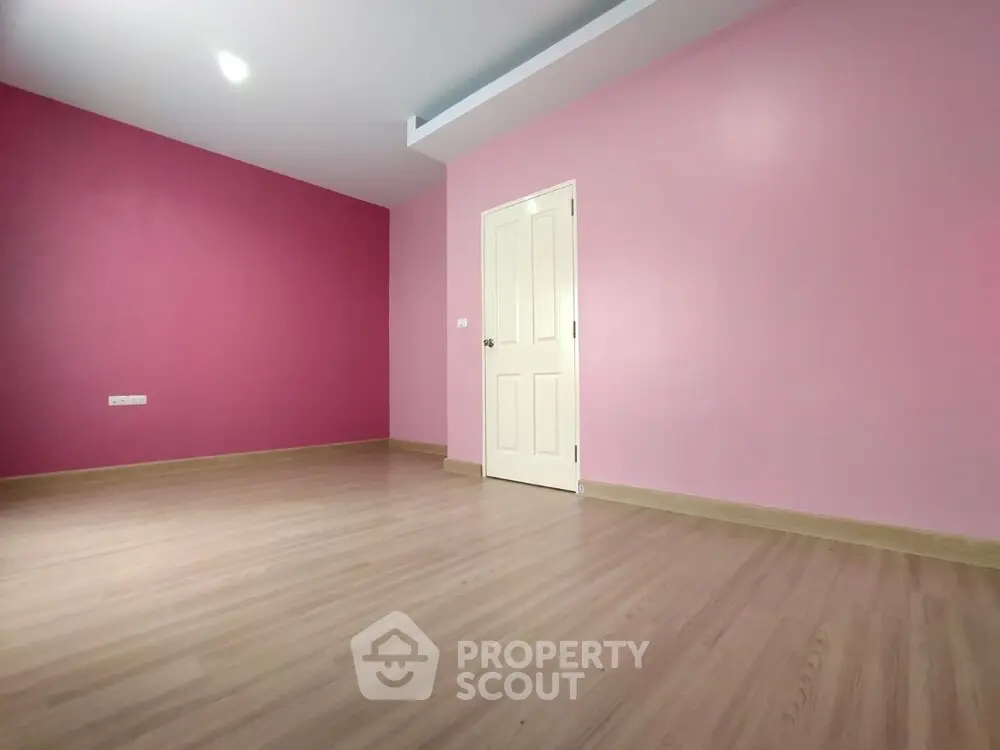 Spacious empty room with pink walls and wooden flooring, ideal for customization.