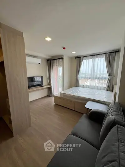 Modern studio apartment with cozy living area and large windows offering natural light.